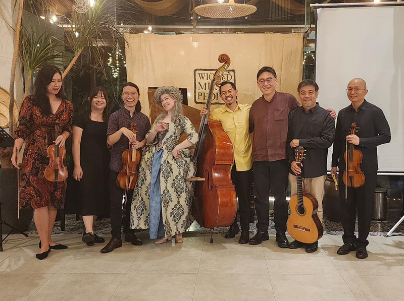 Eight people stand in a row; some of them are holding instruments