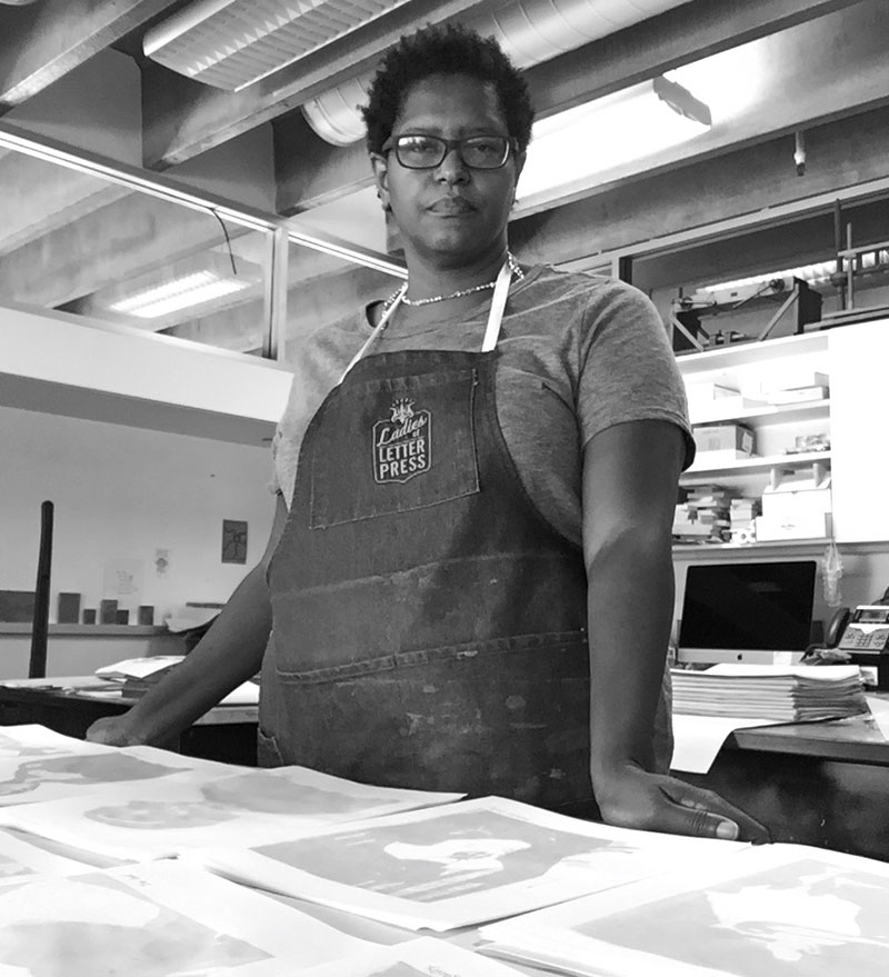 Tia Blassingame stands in front of a table of prints in a studio