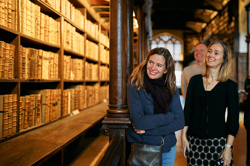 Two women and a man look at shelves of very old books inside an old library