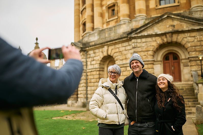 Three people in warm clothing pose for a photo outside the Radcliffe Camera
