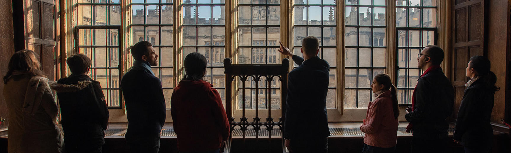 A silhouette of a group looking out of a large window with individual panes separated by lead