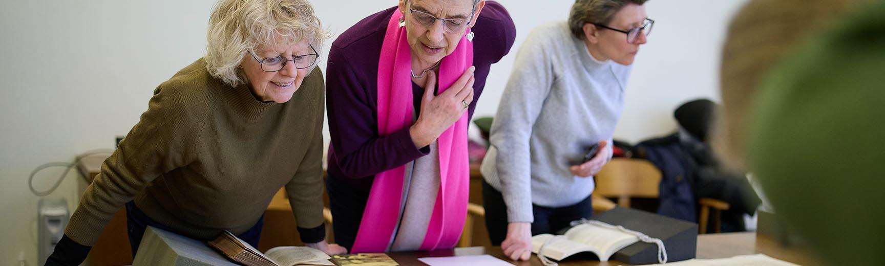 Three women lean over a table to examine rare books