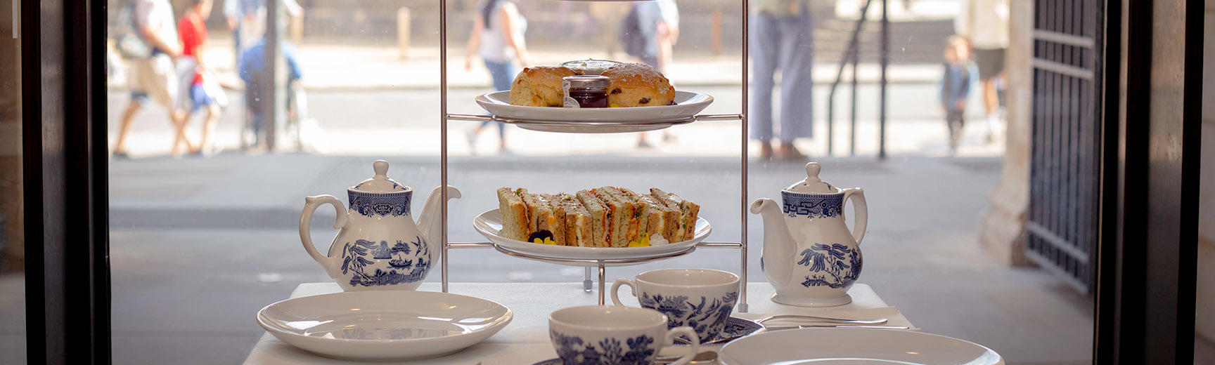 A table laid for afternoon tea with blue and white china and a tiered cake stand of sandwiches and cakes