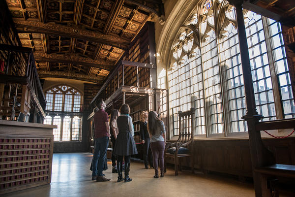 A tour group stands in the historic Duke Humfrey's Library, looking at a window