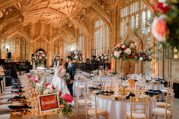 A couple in their bridal outfits stand between tables decorated with lights in the Divinity School at the Bodleian