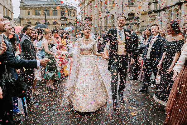 A bride and groom walk through a shower of confetti