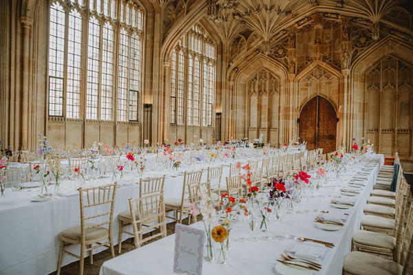Two long tables laid for a wedding: with a white table cloth and red flowers in vases