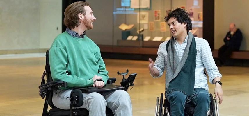 Two people in wheelchairs speak to each other in a large hall