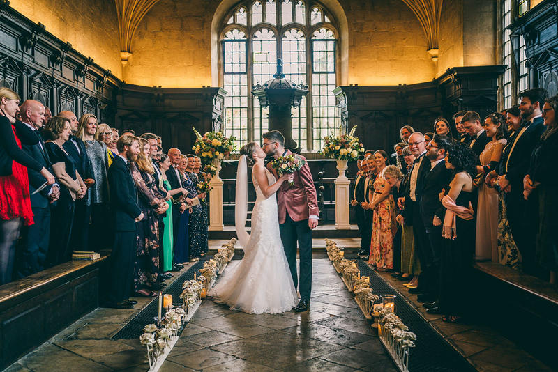 A bride and groom kiss in front of a crowd at their wedding ceremony at the Bodleian Library