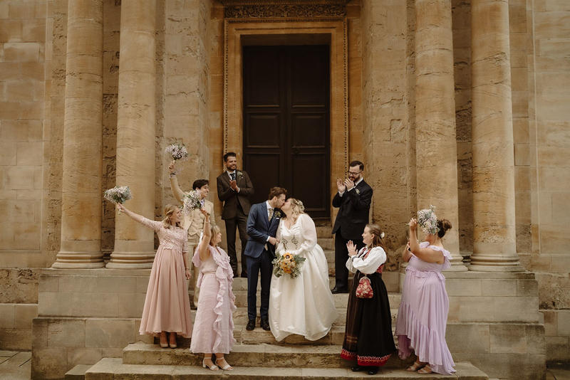 A bride and groom surrounded by three bridesmaids in purple and two groomsmen in suits on the steps outside the Bodleian Library