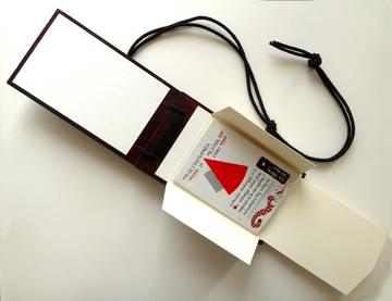 A foldout paper book on a cardboard back with text and red detail